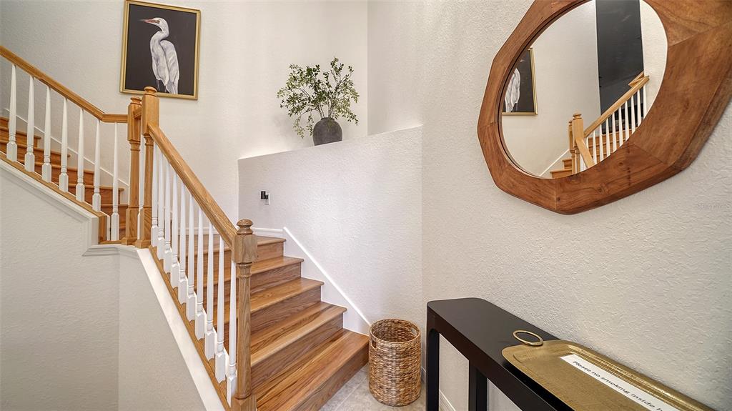 A wooden staircase with white railings leads upward next to a console table and mirror — 6512 GRAND ESTUARY TRAIL UNIT 102, BRADENTON, FL