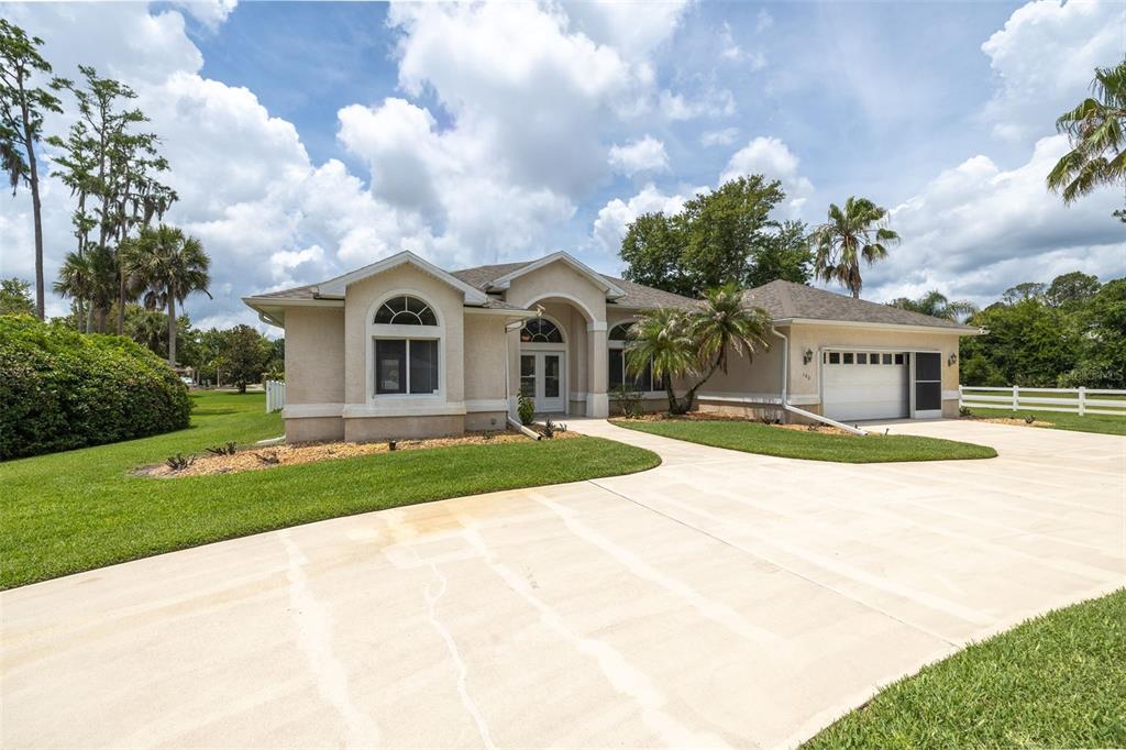 A single-story beige house with a concrete driveway, a two-car garage, and a large lawn — 100 PARADISE VALLEY COURT, DAYTONA BEACH, FL