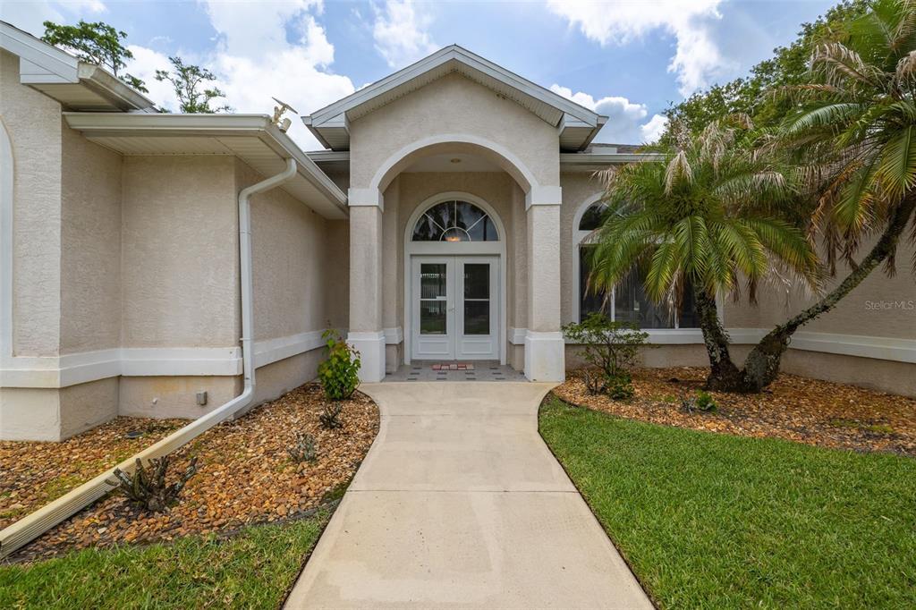 A concrete walkway leads to the arched entryway and double front doors of a house — 100 PARADISE VALLEY COURT, DAYTONA BEACH, FL