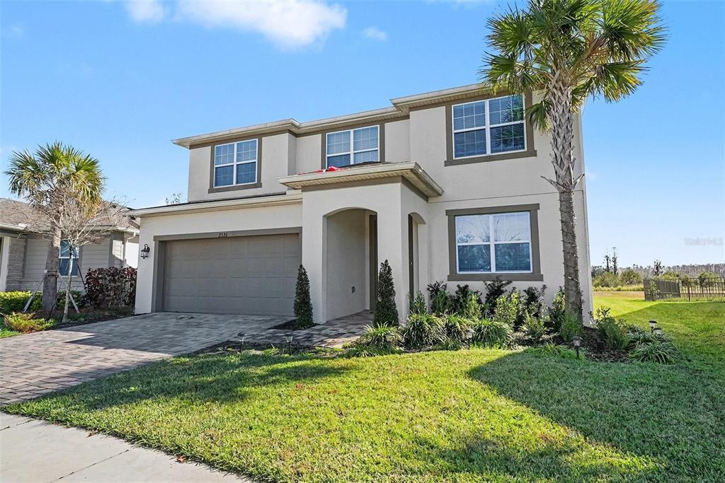 A two-story suburban house with a beige stucco exterior, a two-car garage, and palm trees — 2326 VILLAGE AMBLE LOOP, LUTZ, FL