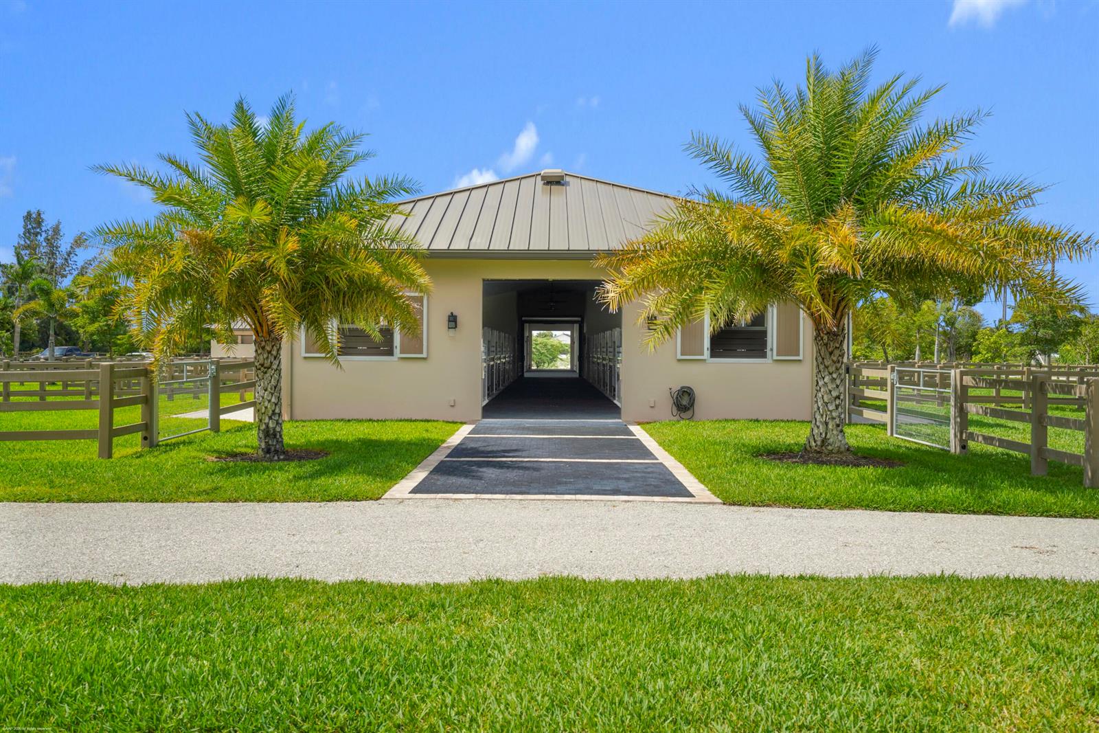 A tan stable building with a metal roof is flanked by two palm trees — 16219 Hollow Tree Lane, Wellington FL 33470, WELLINGTON, FL