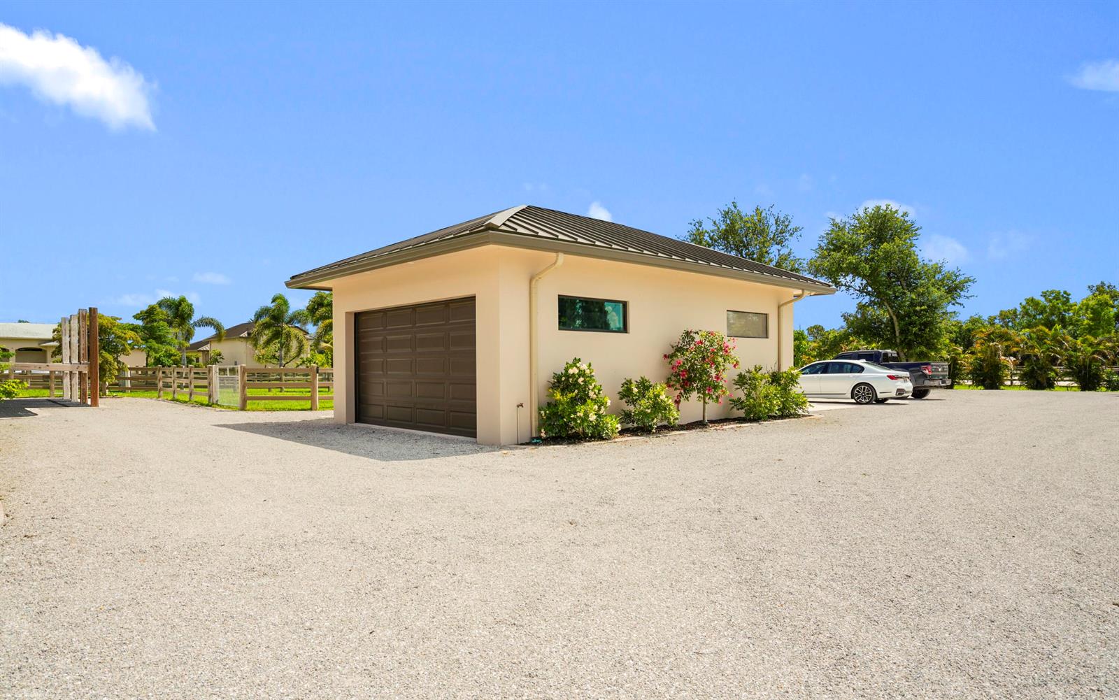 A detached garage with a metal roof sits on a gravel lot near parked cars — 16219 Hollow Tree Lane, Wellington FL 33470, WELLINGTON, FL