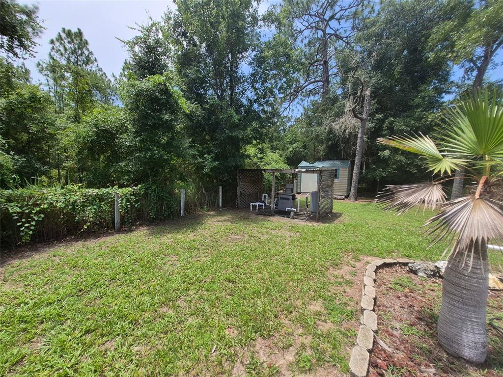 A backyard features a grassy lawn, a small shed, and a covered utility structure — 9 TEAK WAY DRIVE, OCALA, FL
