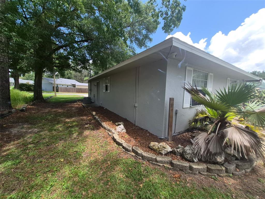 The side exterior of a gray house features a stone garden border and landscaping — 9 TEAK WAY DRIVE, OCALA, FL