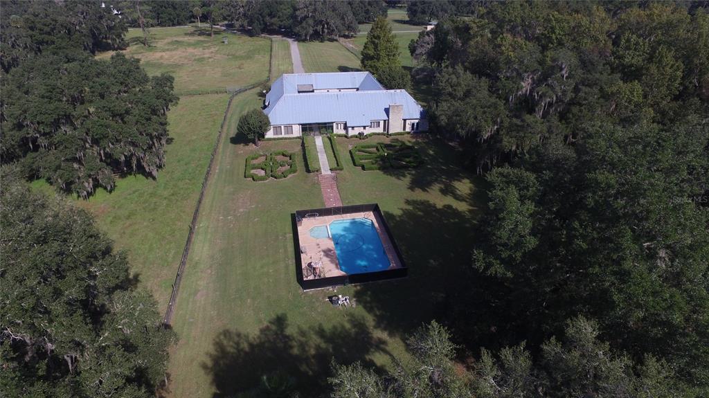 An aerial view shows a house with a metal roof, a pool, and landscaped gardens — 19350 NW 123RD COURT, MICANOPY, FL