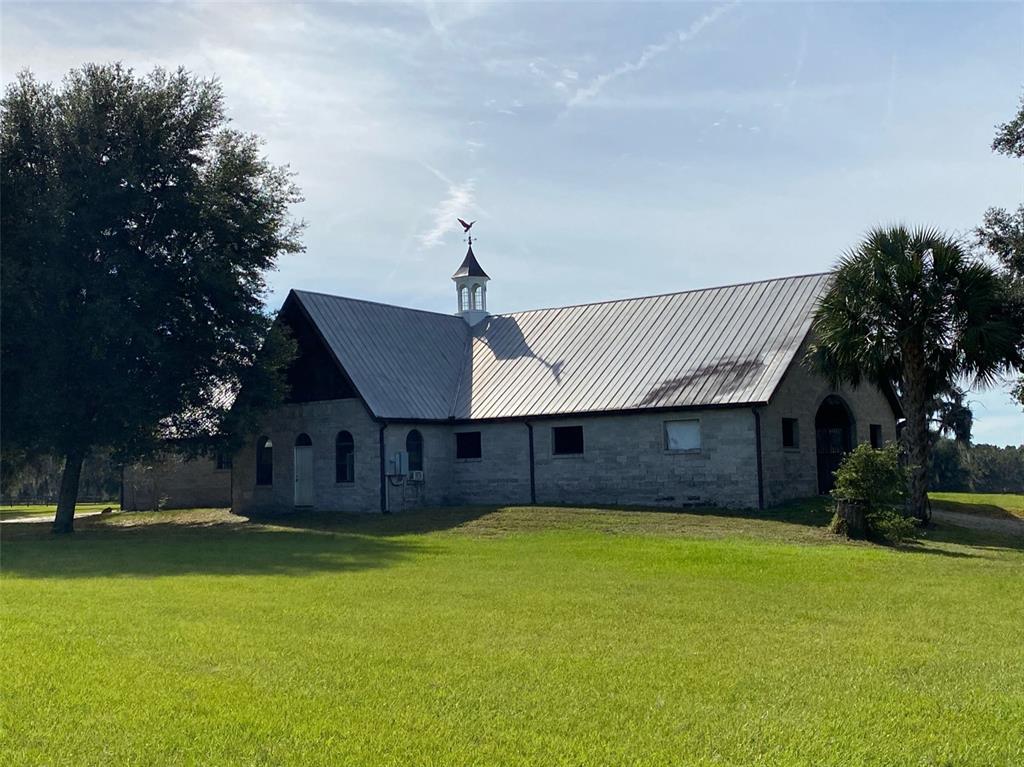 A stone building with a metal roof and a cupola sits on a grassy lawn — 19350 NW 123RD COURT, MICANOPY, FL