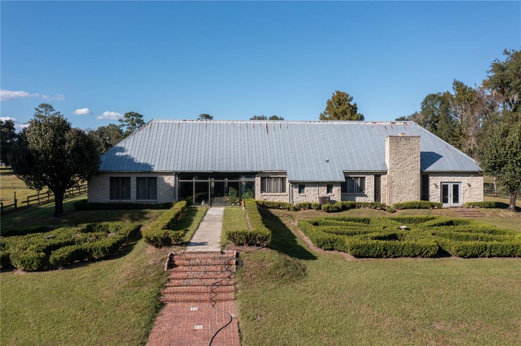 A stone house with a metal roof features a formal hedge garden and brick walkway — 19350 NW 123RD COURT, MICANOPY, FL