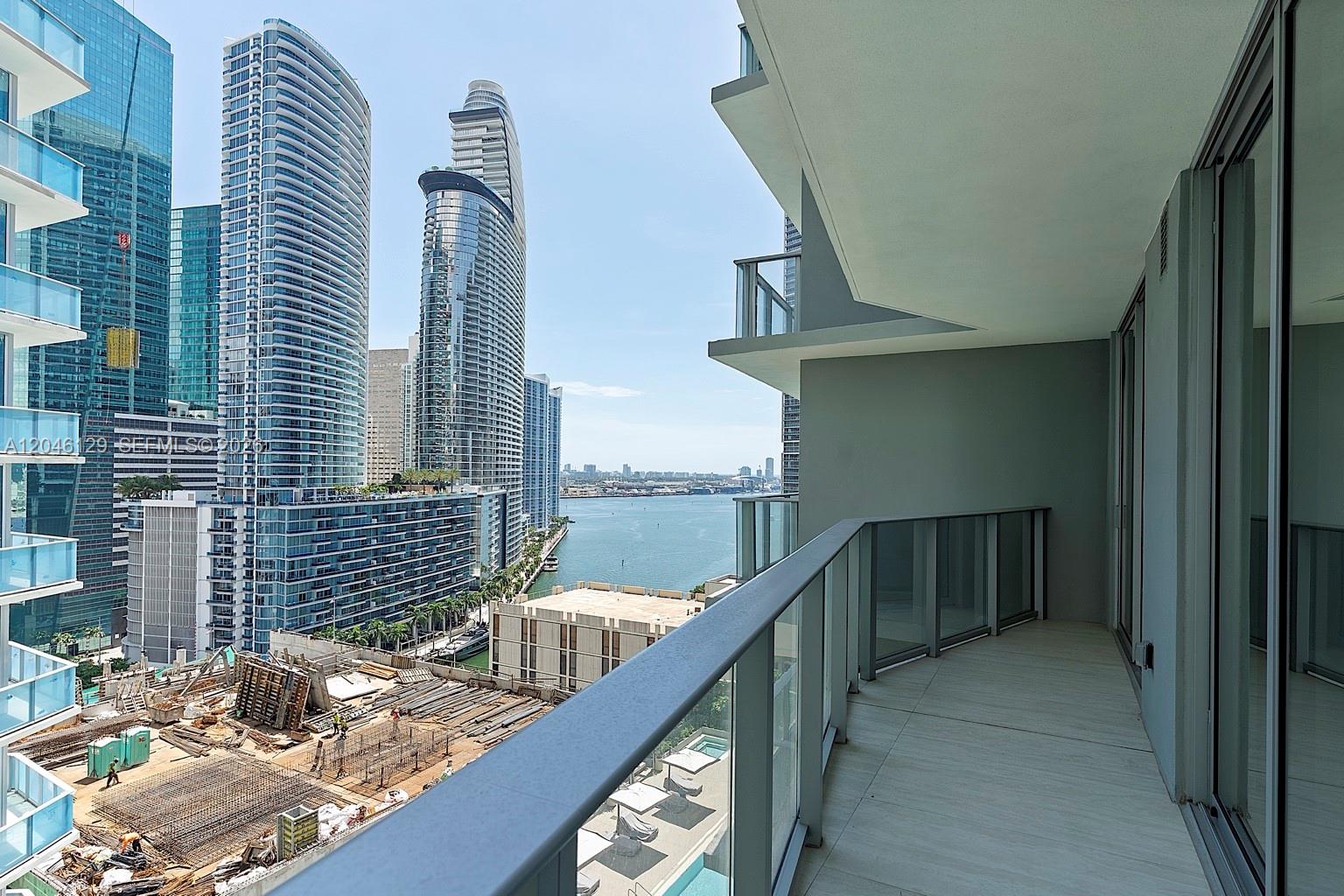 A balcony with glass railings overlooks a construction site, city skyscrapers, and a bay — 77 SE 5th St. # 1905, Miami FL 33131, MIAMI, FL