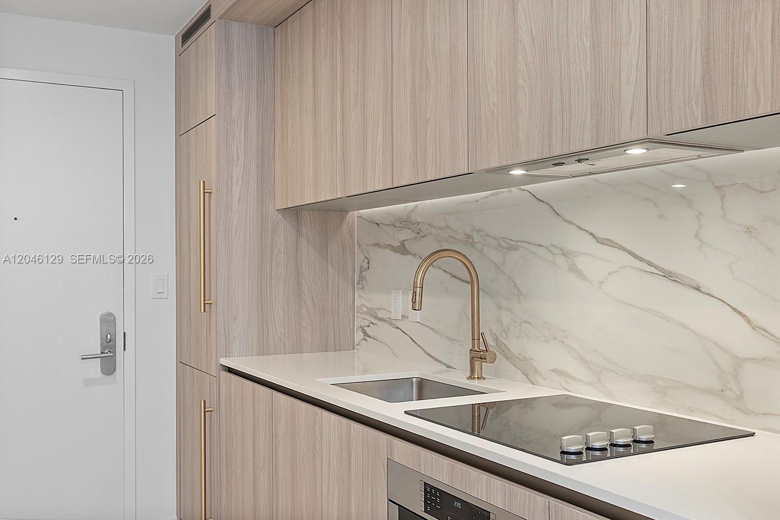 A modern kitchen features light wood cabinetry, a marble backsplash, and a gold faucet — 77 SE 5th St. # 1905, Miami FL 33131, MIAMI, FL