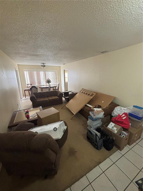 A living room with beige carpet, tan walls, and a dining area in the background — 2709 E 122ND AVENUE, TAMPA, FL