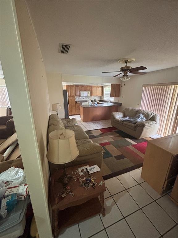 A living room with tile floors and a ceiling fan opens into a kitchen area — 2709 E 122ND AVENUE, TAMPA, FL
