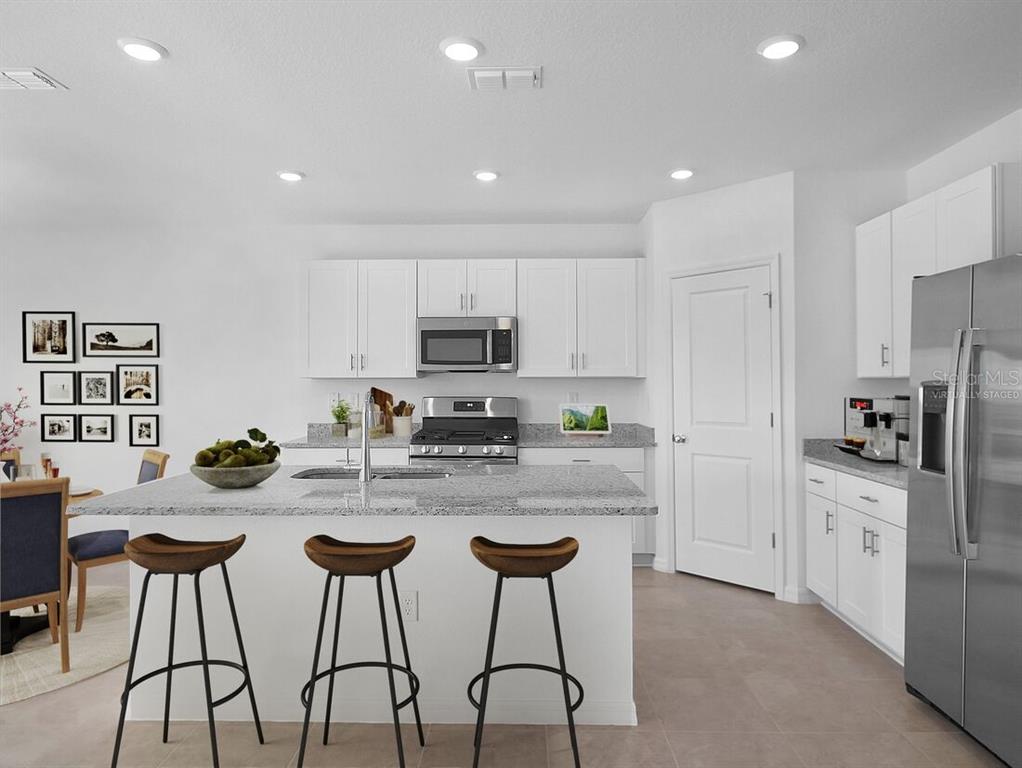 A modern kitchen features white cabinetry, granite countertops, a center island, and three bar stools — 13818 SAWMILL STREET, PARRISH, FL