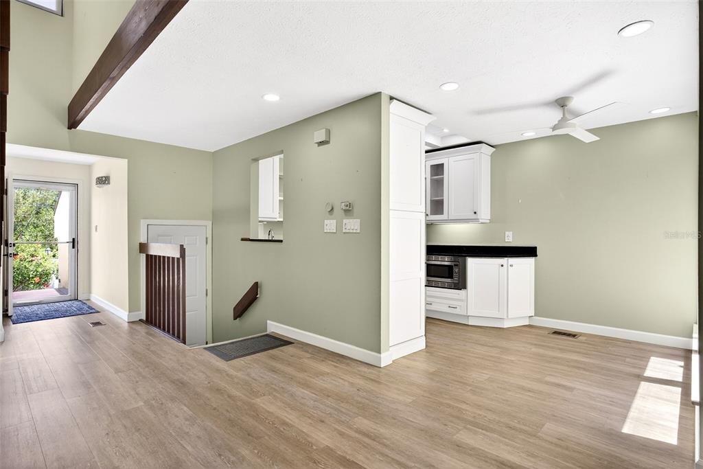 A kitchen with white cabinets and light wood flooring opens to a staircase and entryway — 25188 MARION AVENUE UNIT 1006, PUNTA GORDA, FL