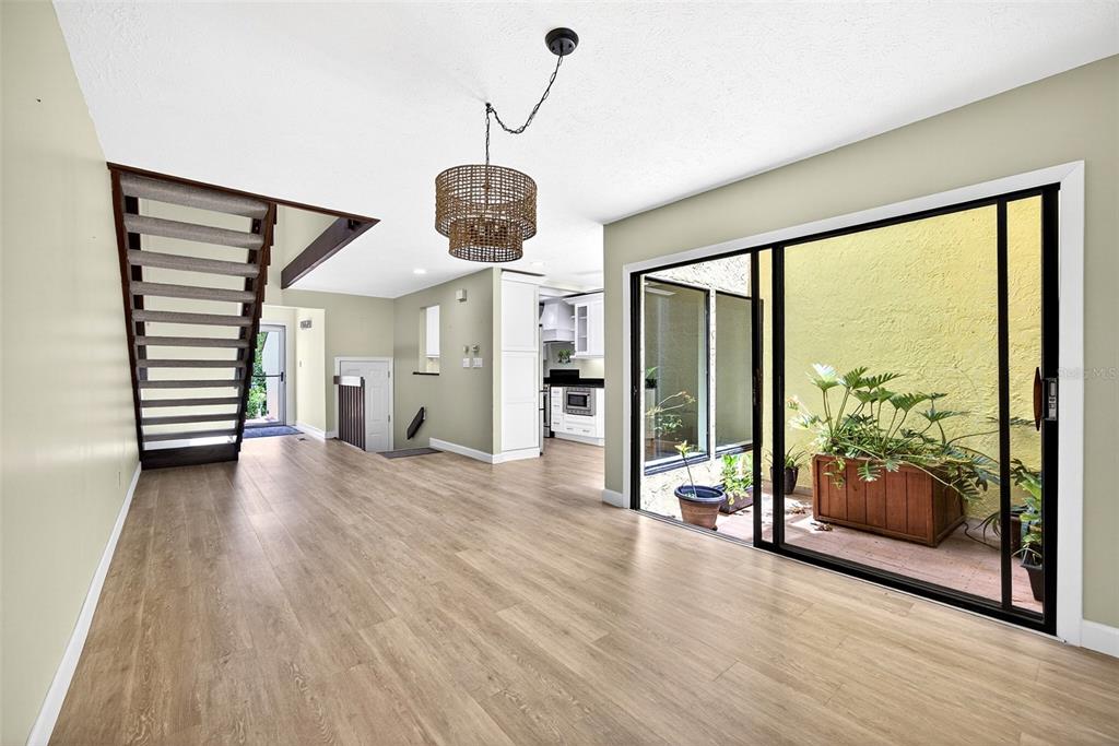 A living area with light wood floors, a staircase, and sliding glass doors to a courtyard — 25188 MARION AVENUE UNIT 1006, PUNTA GORDA, FL