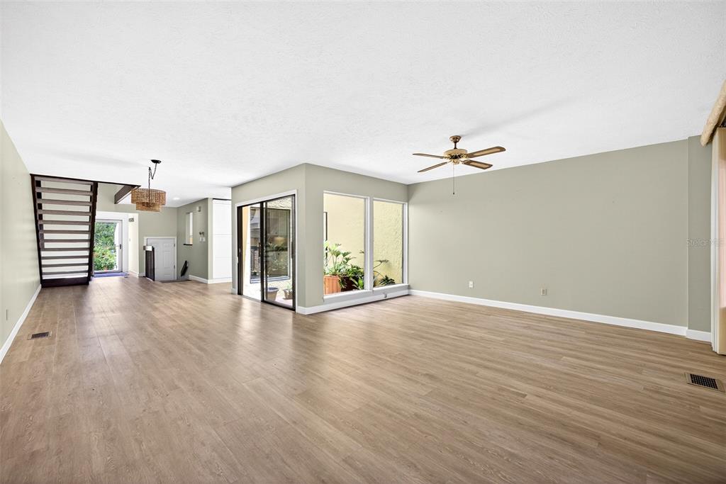 A spacious living room features light wood-look flooring, a ceiling fan, and a staircase — 25188 MARION AVENUE UNIT 1006, PUNTA GORDA, FL