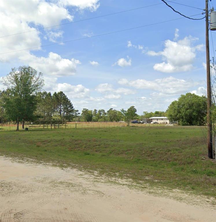 A grassy, vacant lot is bordered by a dirt road, trees, and a utility pole — 109 MAHOGANY LANE, INTERLACHEN, FL