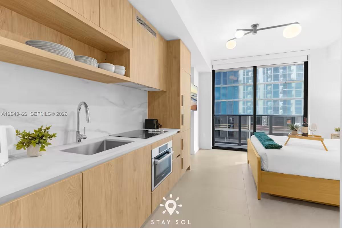 A studio apartment features a modern kitchenette with light wood cabinets and a bed — 11 NE 6th St # 1606, Miami FL 33132, MIAMI, FL