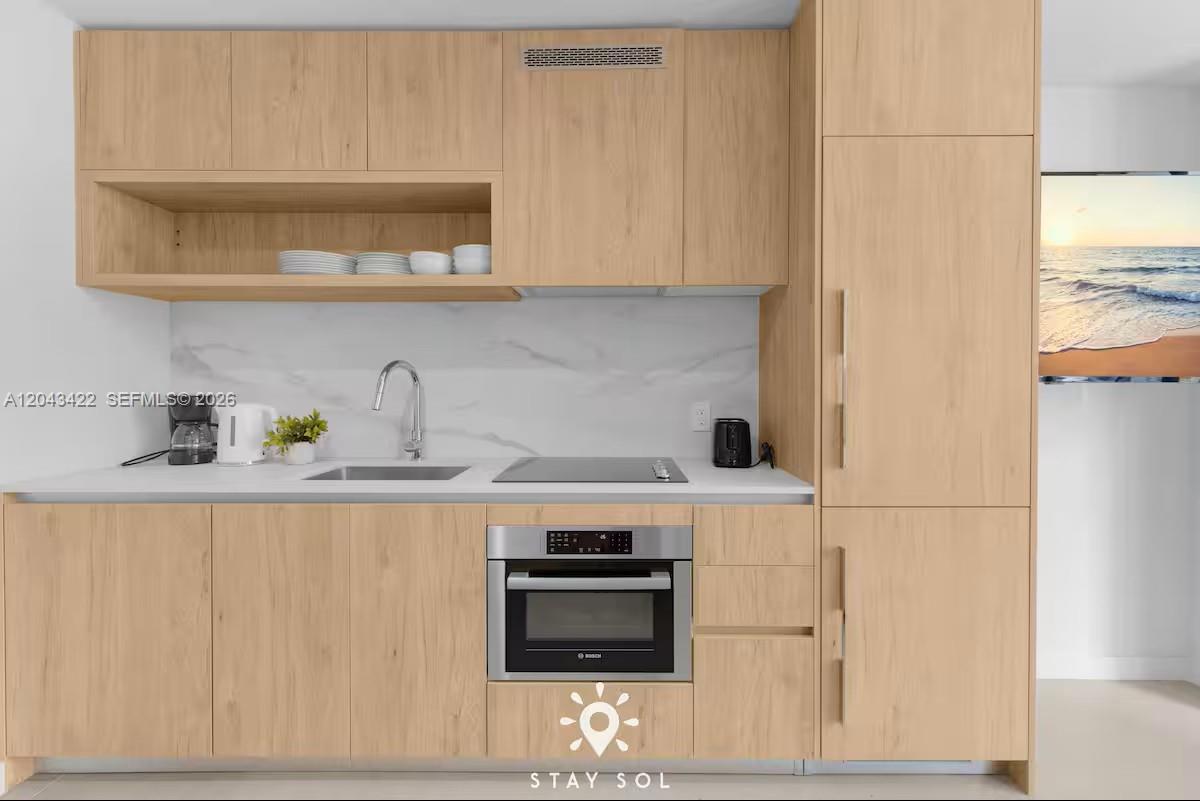 A modern galley kitchen features light wood cabinetry, white countertops, and a stainless steel oven — 11 NE 6th St # 1606, Miami FL 33132, MIAMI, FL
