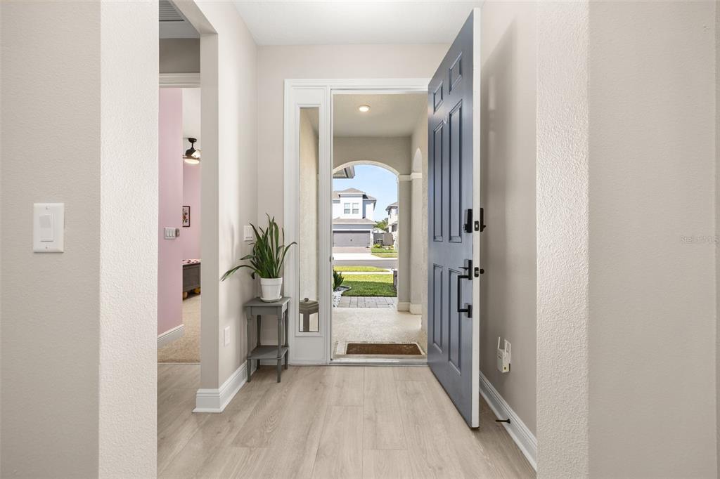 An entryway with light wood-look flooring, a blue front door, and a small side table — 4542 LIONS GATE AVENUE, CLERMONT, FL