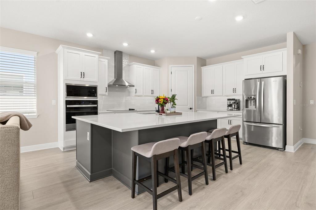 A modern kitchen features a large gray island, white cabinetry, stainless steel appliances, and light flooring — 4542 LIONS GATE AVENUE, CLERMONT, FL