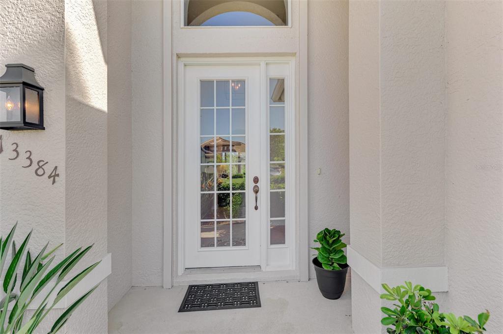 A white front door with glass panels and a sidelight sits under a covered entryway — 13384 GOLF POINTE DRIVE, PORT CHARLOTTE, FL