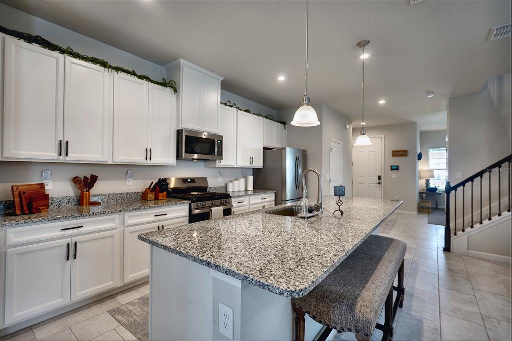 A kitchen features white cabinets, granite countertops, a central island with seating, and stainless appliances — 3922 GREAT SMOKEY WAY, APOPKA, FL