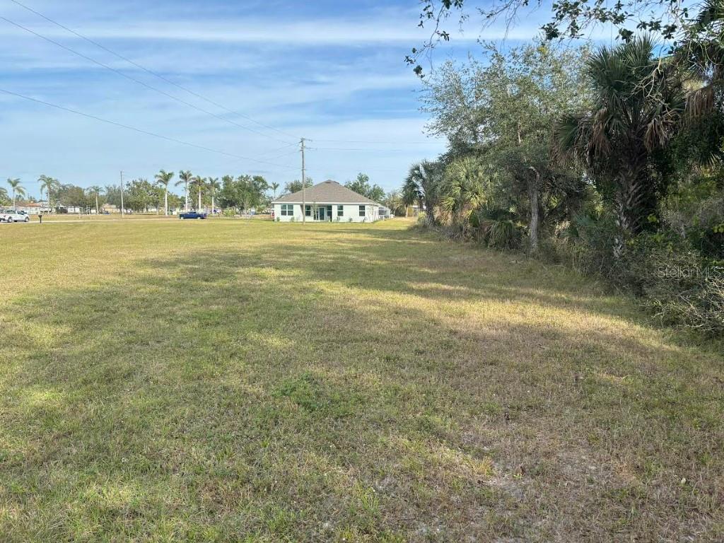 A grassy vacant lot sits in front of a single-story house under a blue sky — 25251 DOREDO DRIVE, PUNTA GORDA, FL