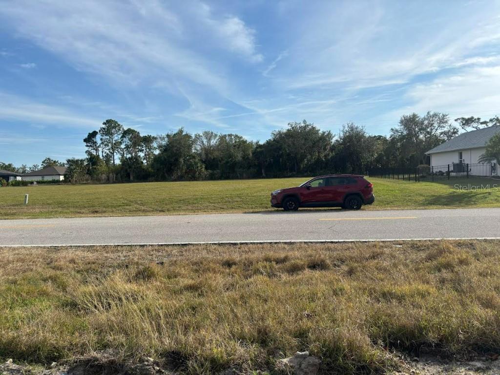 A red SUV is parked on a vacant grassy lot next to a paved road — 25251 DOREDO DRIVE, PUNTA GORDA, FL