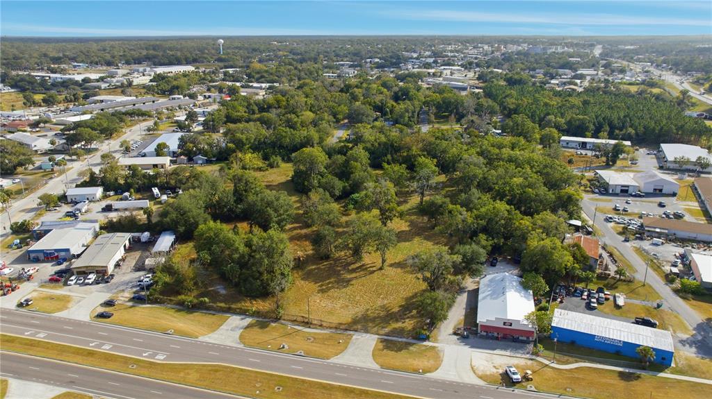 An aerial view shows a vacant, tree-covered lot situated between commercial buildings and a highway — TBD NW 20TH STREET, OCALA, FL