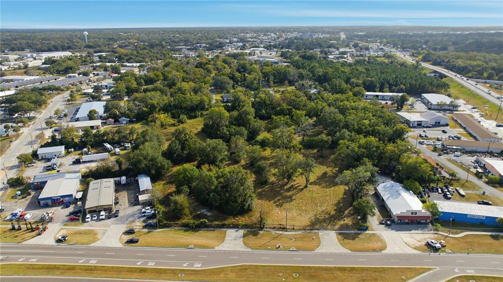 An aerial view shows a vacant, tree-covered lot situated between commercial buildings and a highway — TBD NW 20TH STREET, OCALA, FL