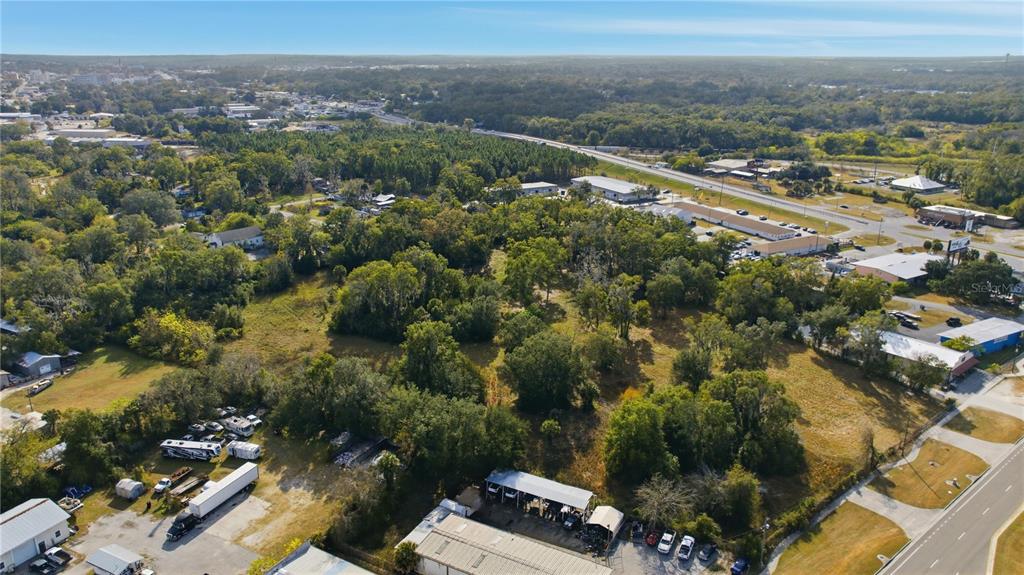 An aerial view shows a large, wooded vacant lot surrounded by commercial buildings and roads — TBD NW 20TH STREET, OCALA, FL