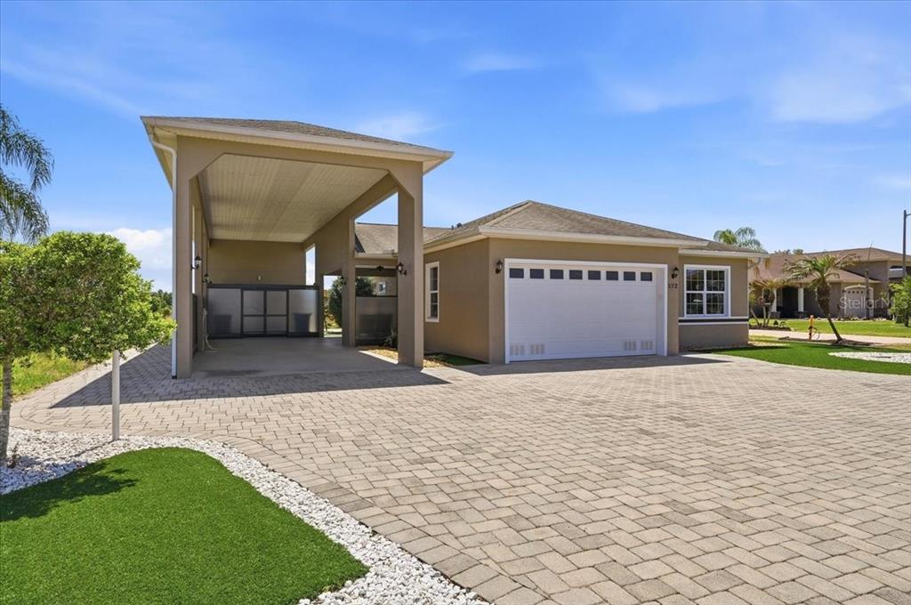 A tan house with a large attached carport and a paved driveway under a blue sky — 572 MEANDERING WAY, POLK CITY, FL