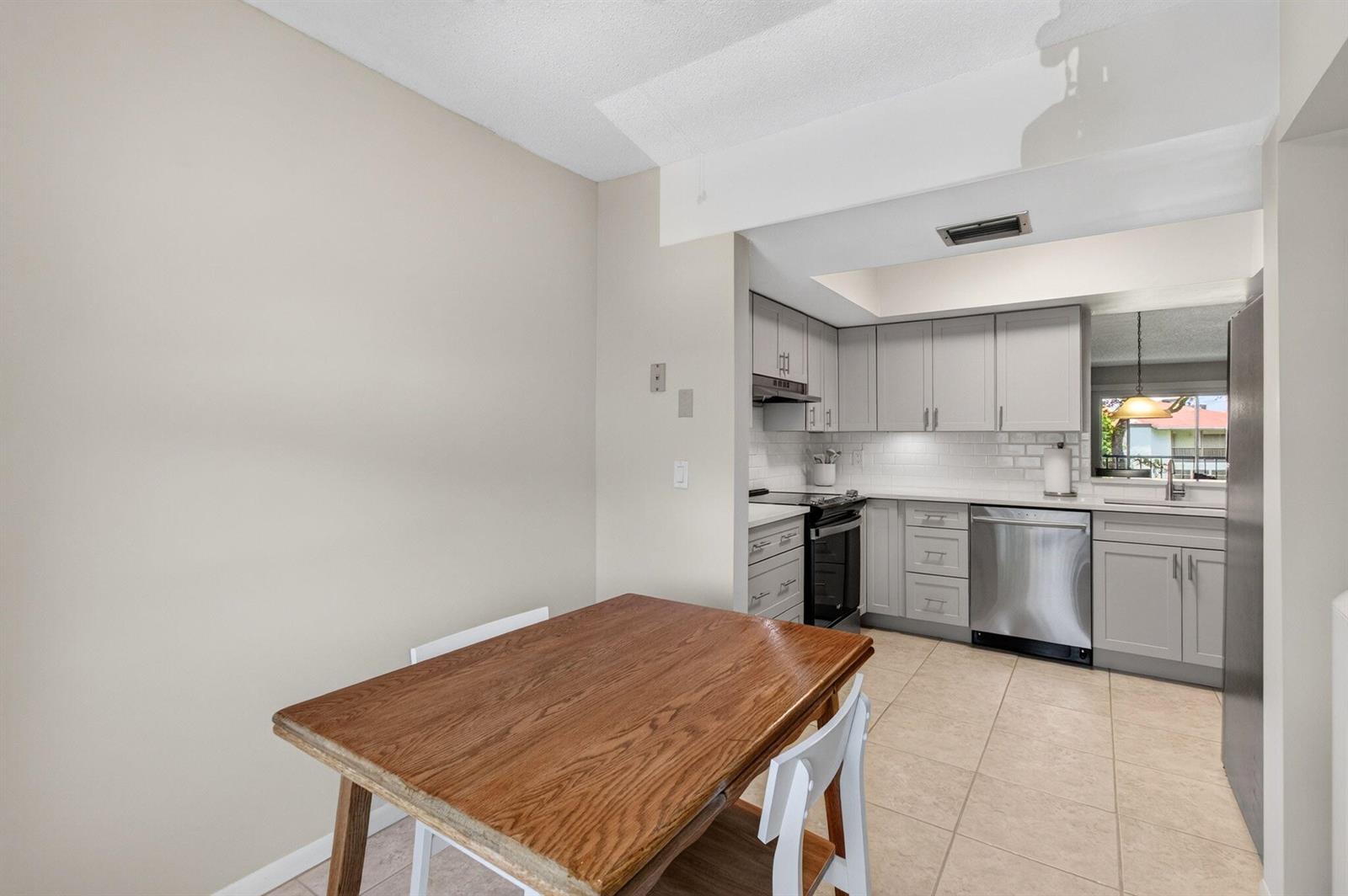 A dining area with a wooden table sits adjacent to a kitchen with gray cabinets — 6600 S Oriole Boulevard, Delray Beach FL 33446, DELRAY BEACH, FL