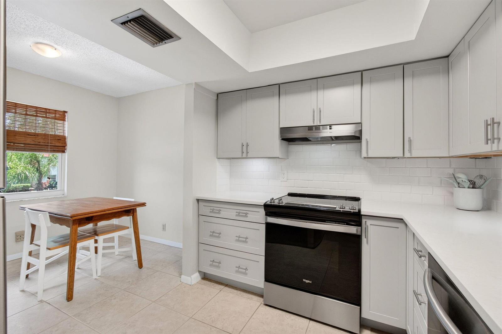 A kitchen features light gray cabinets, white countertops, a subway tile backsplash, and a dining area — 6600 S Oriole Boulevard, Delray Beach FL 33446, DELRAY BEACH, FL