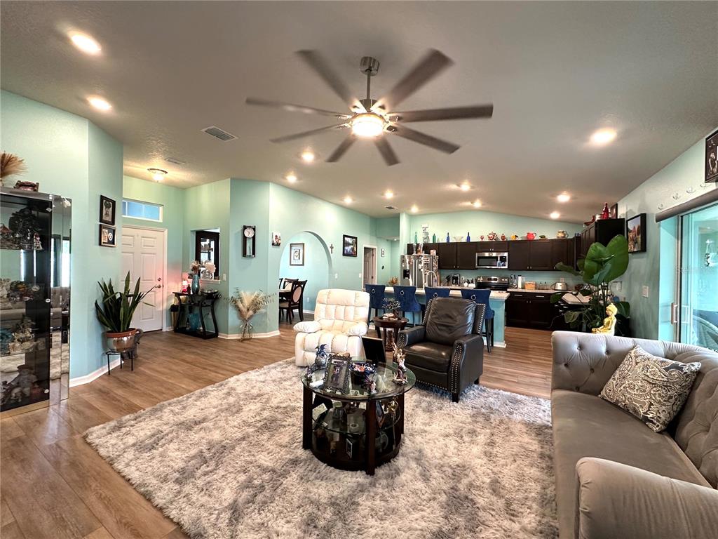 An open-concept living room features light blue walls, wood-look flooring, and a large area rug — 15329 SW 65TH TERRACE ROAD, OCALA, FL