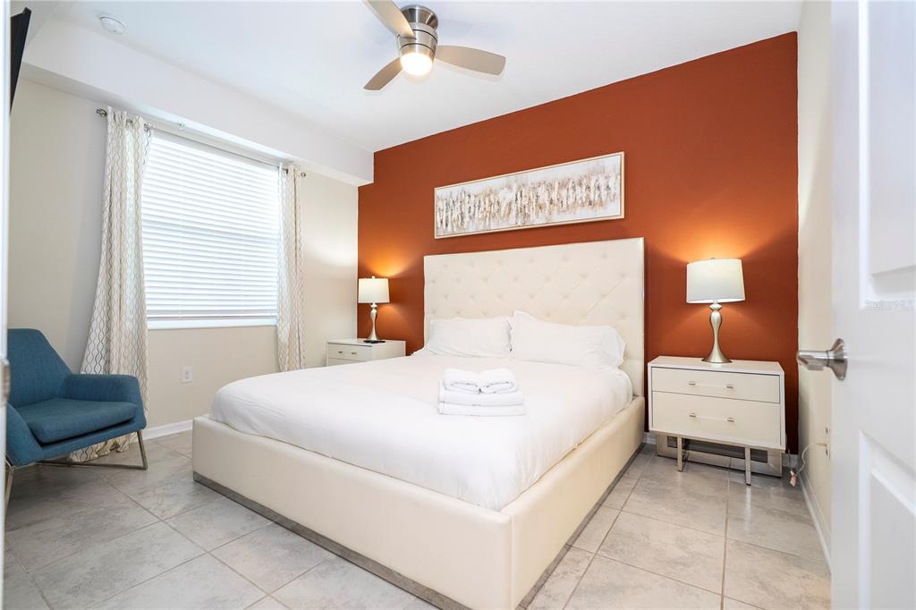 A bedroom features a white upholstered bed, a rust-colored accent wall, and tiled flooring — 3121 PARADOX CIRCLE UNIT 303, KISSIMMEE, FL