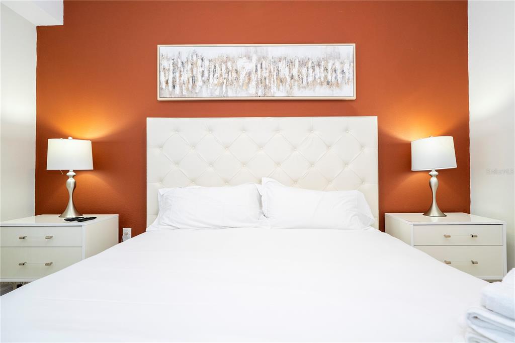 A bedroom features a white tufted headboard against an orange wall with two bedside lamps — 3121 PARADOX CIRCLE UNIT 303, KISSIMMEE, FL