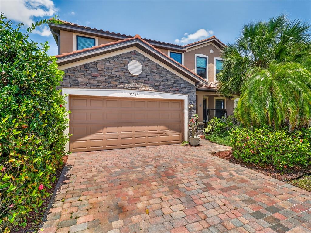 A two-story house with a stone-accented facade, a two-car garage, and a paver driveway — 2740 VIA PIAZZA LOOP, FORT MYERS, FL