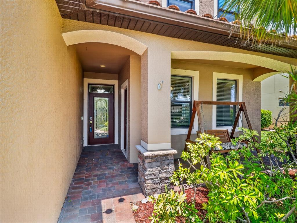 A covered entryway features a brick-paver floor, a wooden porch swing, and a glass-paneled door — 2740 VIA PIAZZA LOOP, FORT MYERS, FL