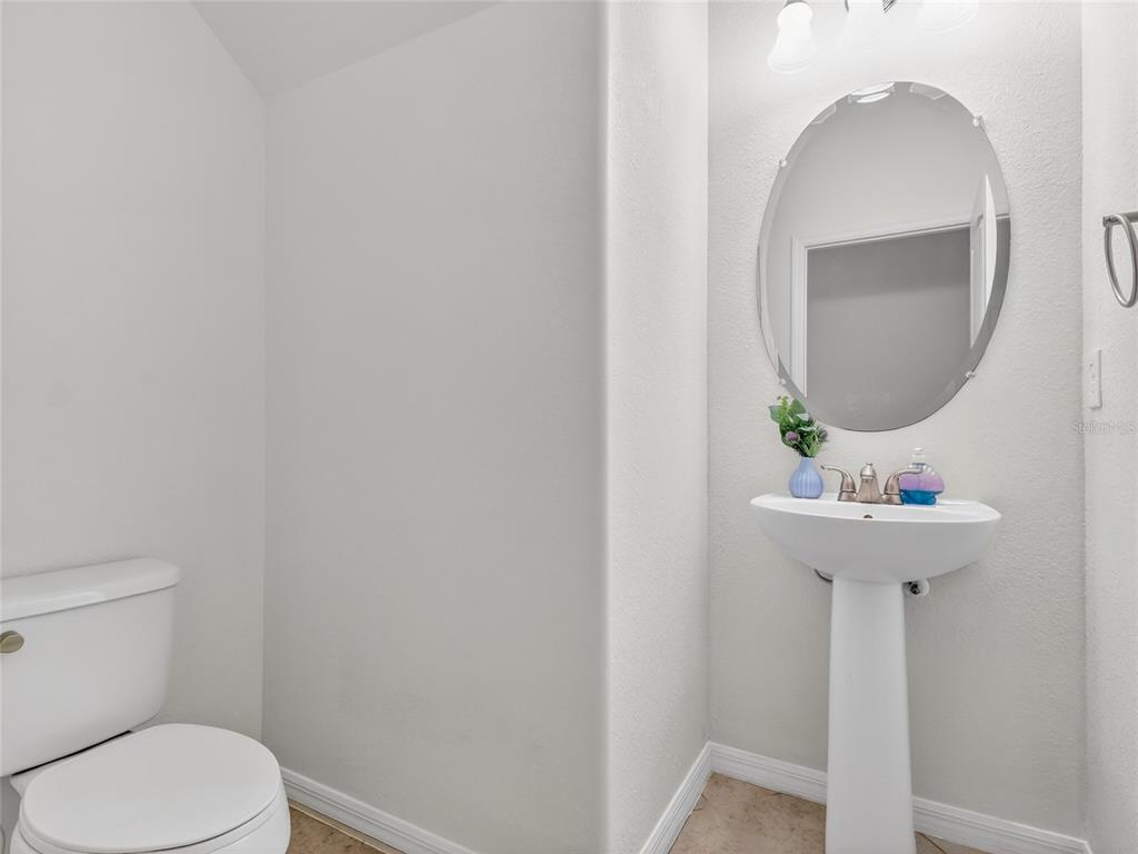A small bathroom features a white pedestal sink, an oval mirror, and a toilet — 2740 VIA PIAZZA LOOP, FORT MYERS, FL