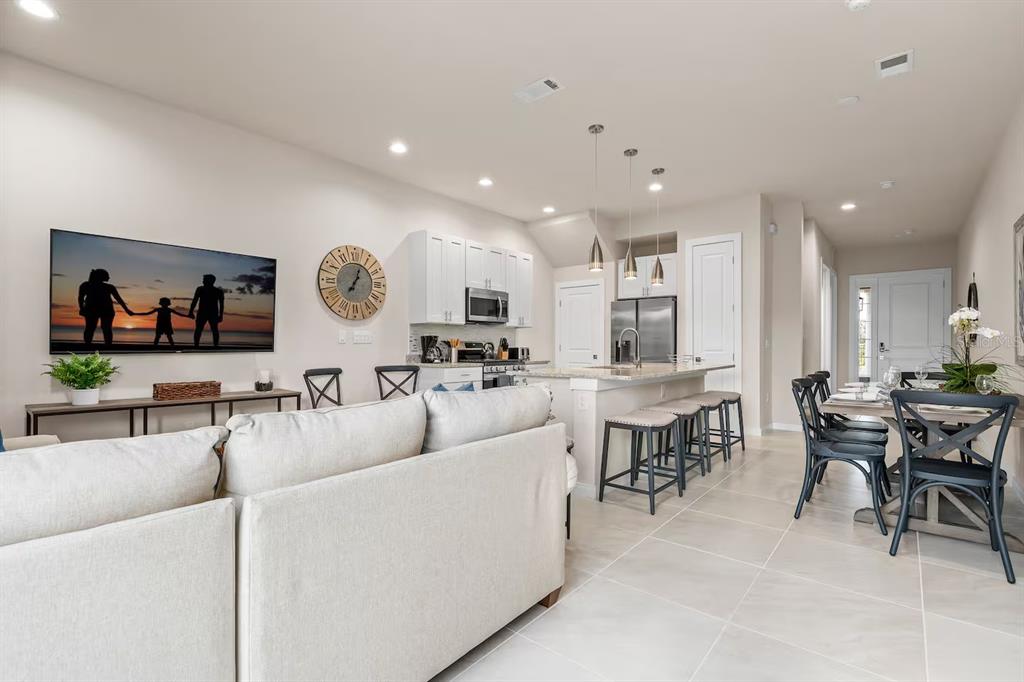 An open-concept living room and kitchen featuring light tile floors, white cabinets, and bar seating — 7568 SUNFLOWER CIRCLE, KISSIMMEE, FL