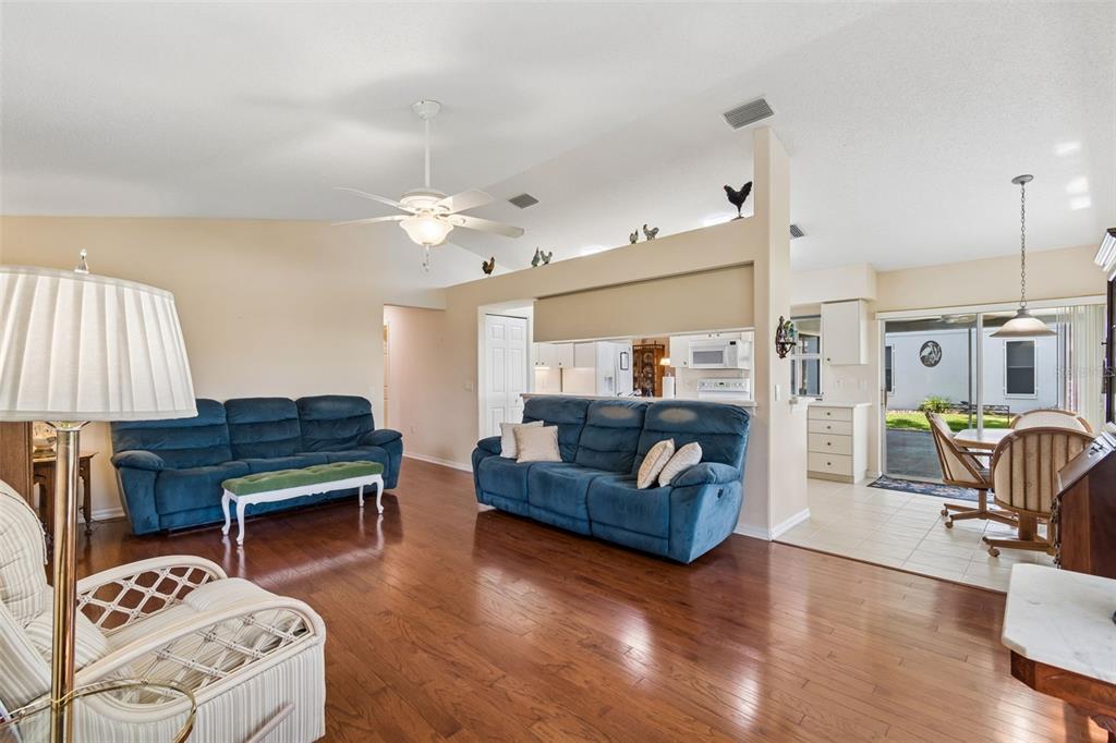 A living room with blue sofas, hardwood floors, and an open kitchen area — 18508 GRAND CLUB DRIVE, HUDSON, FL