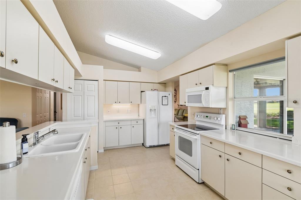 A kitchen features white cabinetry, white appliances, a double sink, and a window with outdoor views — 18508 GRAND CLUB DRIVE, HUDSON, FL