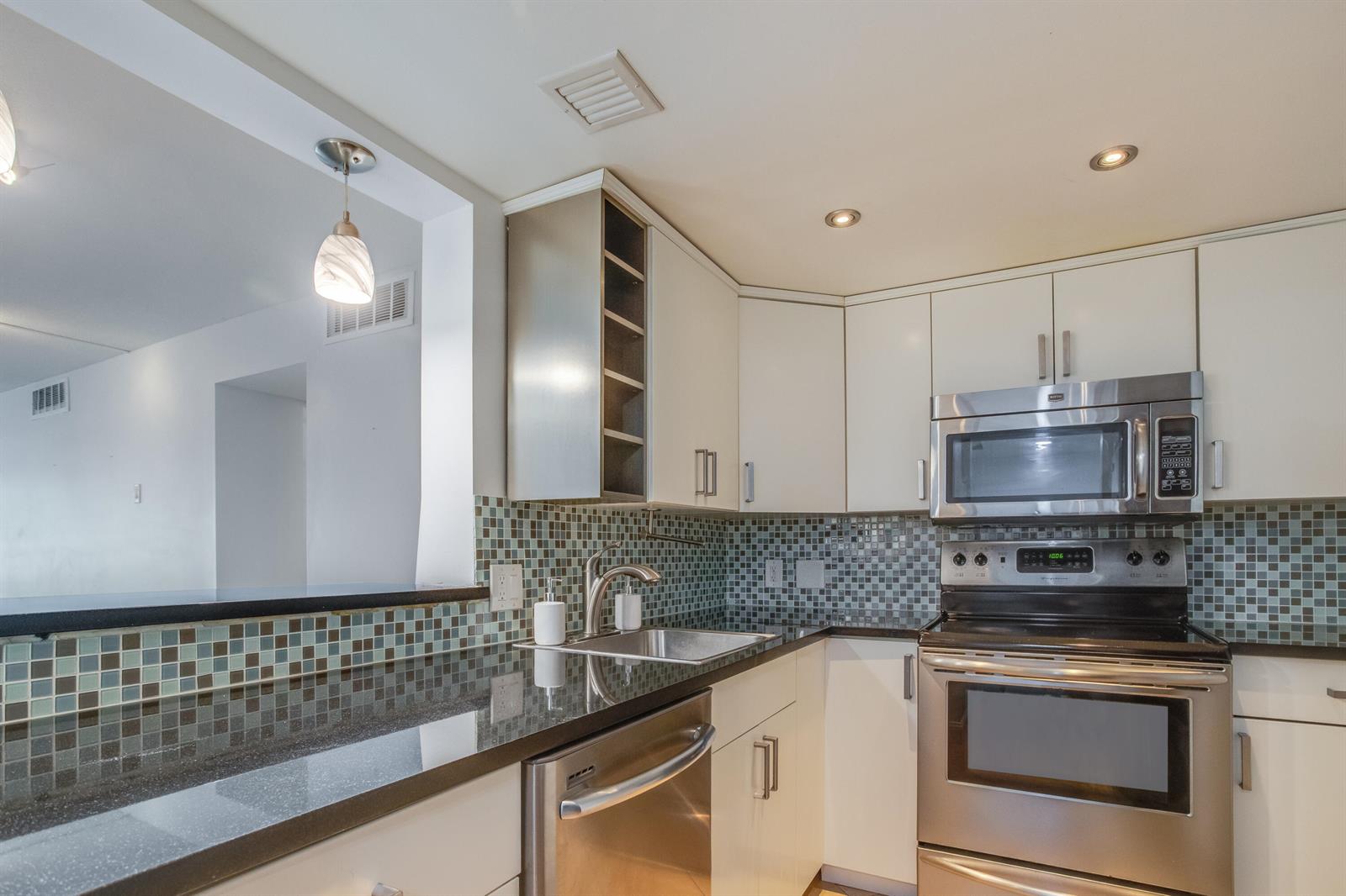 A kitchen features white cabinets, stainless steel appliances, a black countertop, and a mosaic backsplash — 2651 S Course Drive # 109, Pompano Beach FL 33069, POMPANO BEACH, FL