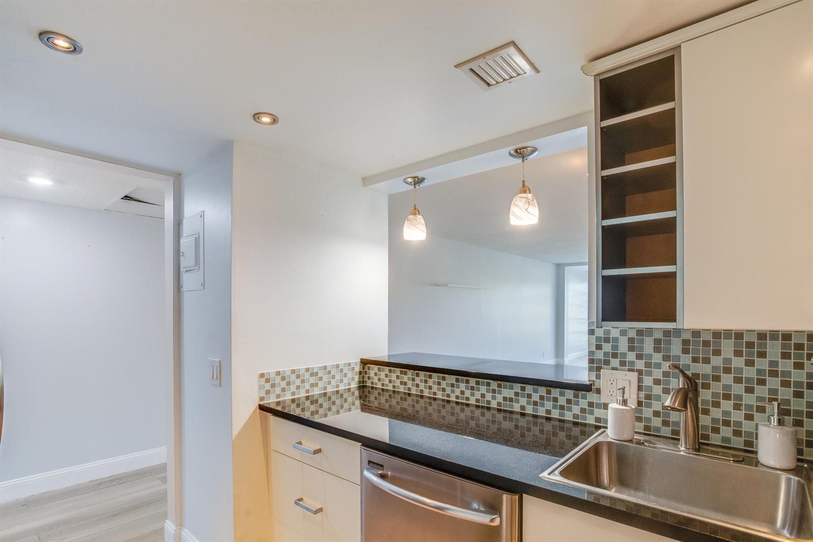 A kitchen features dark granite countertops, a stainless steel sink, and a mosaic tile backsplash — 2651 S Course Drive # 109, Pompano Beach FL 33069, POMPANO BEACH, FL