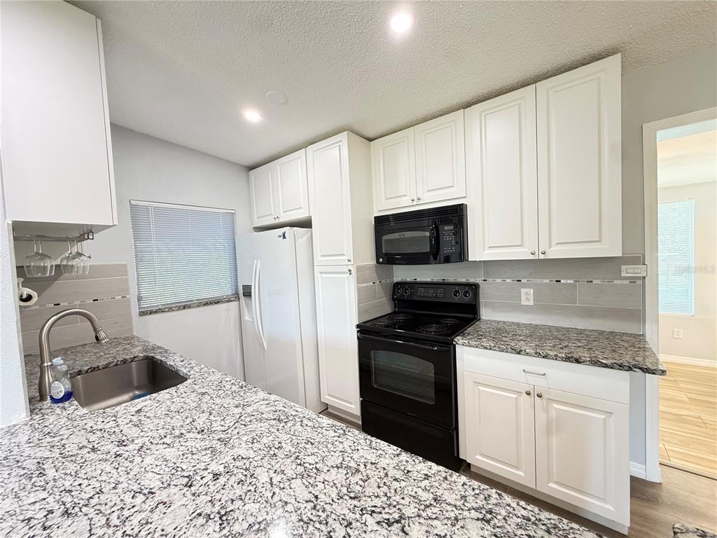 A kitchen features white cabinets, granite countertops, a stainless steel sink, and black appliances — 351 PALMETTO DRIVE NE, PORT CHARLOTTE, FL