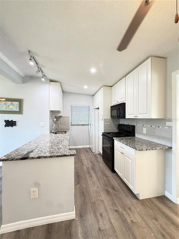 A kitchen features white cabinets, granite countertops, black appliances, and wood-look flooring — 351 PALMETTO DRIVE NE, PORT CHARLOTTE, FL