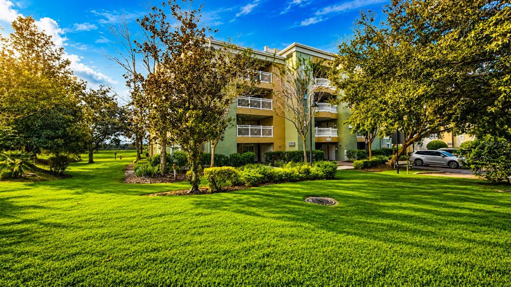 A multi-story apartment building with balconies sits behind a large, manicured green lawn — 1370 CENTRE COURT RIDGE DRIVE UNIT 303, REUNION, FL