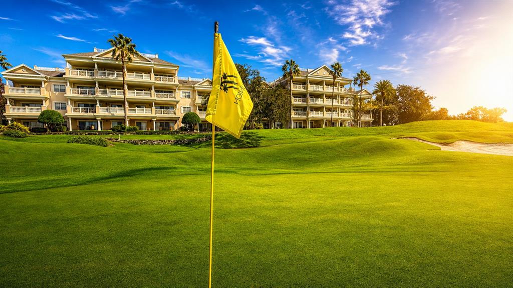 A yellow golf flag stands on a green in front of a large resort building — 1370 CENTRE COURT RIDGE DRIVE UNIT 303, REUNION, FL