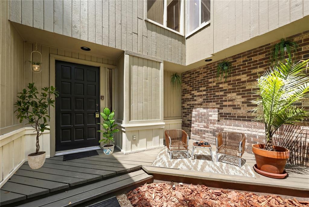 A wooden deck entryway features a black front door, brick wall, and two patio chairs — 548 S OSCEOLA AVENUE, ORLANDO, FL